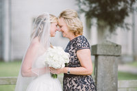 Mother of bride and bride stand forehead to forehead on wedding day
