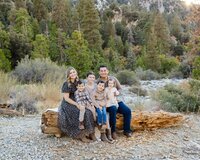 Family of six sitting on a log outdoors in a forest setting during a natural light family photography session in Yucaipa with Kaitlyn Dawn Photography.