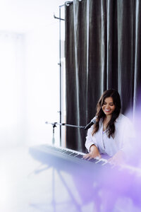 Singer-songwriter performing at a piano and microphone in soft atmospheric light