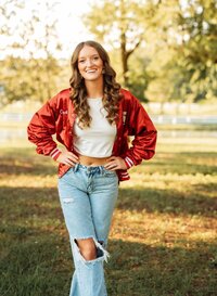 Senior portrait in downtown Magnolia Springs, Alabama — having a laugh in her dance team jacket hands on hips.