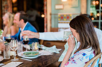 A woman in a floral robe dabs her tears with a napkin at a dinner table