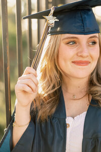 Close-up portrait of a smiling high school graduate wearing a cap and gown, golden hour graduation photography by Kaitlyn Dawn Photography.