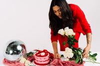 Woman posing with a custom red and pink cake during her colorful brand photography session.