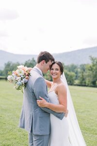 Newlyweds smiling with peach, blue, and white bridal bouquet by Flowergirl Cville, Charlottesville wedding florist, at King Family Vineyard | Photo by Paige Ryan Photography