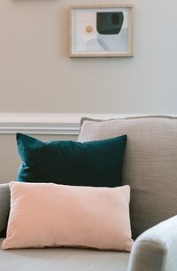 Grey couch with a small pink rectangular pillow and a turquoise square below behind it