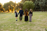Family walking together across a sunlit field during golden hour, candid outdoor family photography by Kaitlyn Dawn Photography.