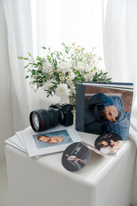 Professional photography setup with camera, newborn albums, and printed images styled with flowers in a bright studio, Kaitlyn Dawn Photography, Yucaipa newborn photographer.