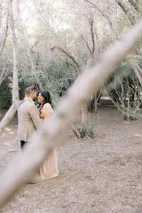 The Dilorio family parents sharing an intimate moment, standing together in a serene wooded setting during a natural light outdoor photography session in Las Vegas.