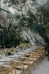 Tablescape in the jungle with light wooden chairs and pink pastel flowers