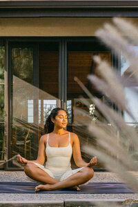 Woman seated on a yoga mat on the patio, framed through garden grasses