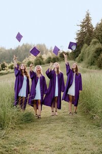 Four high school graduates with purple gowns throwing their caps in the air in a grassy field