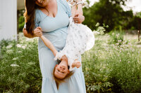 a mother holds her daughter upside down to get some giggles during their family photo session with shelly voss