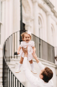 Charleston Baby Milestone Photographer - Toddler gets tossed into the air by her father during Baby Milestone Portraits in downtown Charleston, SC