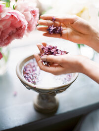 delicate lilac petals and peony held near a decorative water urn in a soft styled detail shot