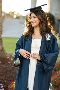 High school graduate wearing a cap and gown looking to the side during an outdoor senior portrait session by Kaitlyn Dawn Photography.