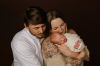 Parents cuddling their newborn baby during a warm studio portrait session. Photographed by Inland Empire newborn photographer Kaitlyn Dawn Photography.