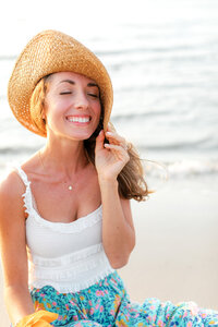 Portrait of a girl sitting on the beach with a floppy beach hat. She is smiling up to the sky.