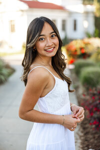 High school senior girl smiling in a garden setting with flowers and greenery, outdoor senior portrait captured by Kaitlyn Dawn Photography.