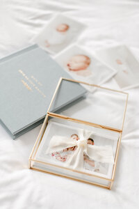 A blue photo album lays under a gold box of photos with a white ribbon around them