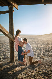Expectant father kissing pregnant mother’s belly during golden hour maternity session on the beach in Atlantic Beach North Carolina
