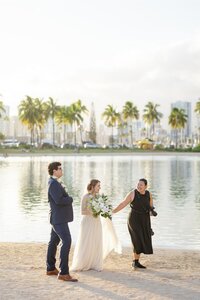 A photographer standing on the beach with a newlywed couple 