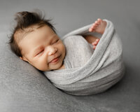 Sleeping newborn baby wrapped in a soft gray swaddle and posed on a neutral backdrop during a studio session with newborn photographer Kaitlyn Dawn Photography.