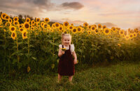 Charleston Baby Milestone Photographer - toddler stands in a field of sunflowers during Baby Milestone Portraits in Charleston, SC.