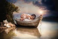 4Karma Studio - A creative fine art newborn portrait featuring a baby sleeping in a wooden boat with a custom-carved name on the bow, captured in true-to-life colors.