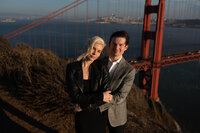 handsome couple casually embracing while overlooking the golden gate bridge from a cliff at sunset