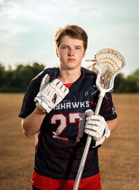 Senior portrait at Battleship Memorial Park in Mobile, Alabama— wearing his lacrosse gear holding a stick.