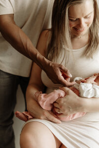 A newborn is gently held by both parents in their Maine home. Fine art lifestyle family photography by Damini Photography capturing tender, intimate, and heartfelt family moments.