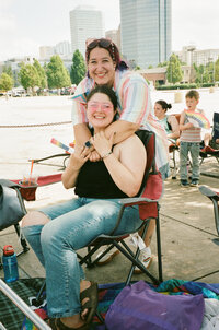 A person with their arms wrapped around another person who is sitting down.