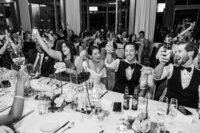 Black and white image of bride and groom raising their drinks for a toast at their wedding reception at The Marion. Captured by Canberra wedding photographer, Acacia & Grace Photography