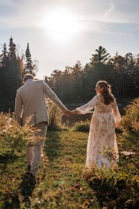 Bride and groom holding hands while walking through a sunlit field during their New England wedding.