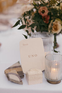 Table number printed on handmade paper being held by a travertine stone, next to broken tiles for an ikebana inspired wedding concep