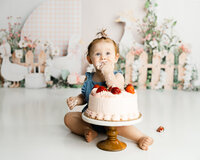 Baby celebrating their first birthday with a strawberry cake during a bright studio cake smash session. Photographed by Yucaipa baby photographer Kaitlyn Dawn Photography.
