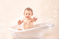 smiling toddler in white baby tub with bubbles after cake smash