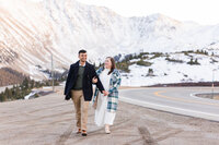 Winter Colorado engagement session—couple walking hand-in-hand with snowy Loveland Pass mountain peaks behind them.