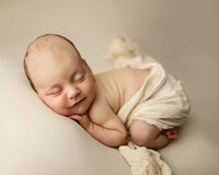 Sleeping newborn baby posed on a neutral blanket with soft natural tones during a studio session by newborn photographer Kaitlyn Dawn Photography.