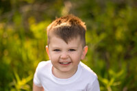 A toddler stands in a Pewaukee meadow and gives a big CHEESE to Kara Reese while she takes his portrait.