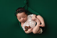 Newborn Girl on green holding a gingerbread man during her newborn session at Jennifer Brandes Photography.