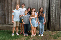 Grandmother standing with her grandchildren in front of a rustic wooden barn during an extended family photo session