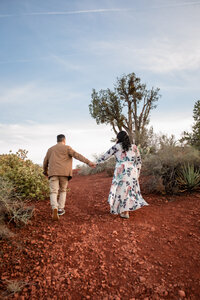 Couple walking hand-in-hand through Sedona's red rock desert landscape