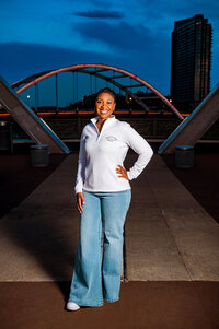 Lipscomb senior wearing jeans and a white shirt standing on the pedestrian bridge at sunset