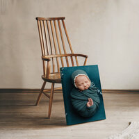 Framed newborn portrait on canvas leaning against a wooden chair in a neutral studio setting, Kaitlyn Dawn Photography, Yucaipa newborn photographer.