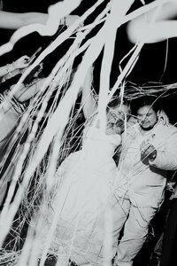 A couple running through a wall of white streamers during their send off at the end of their wedding day edited in black and white with flash.