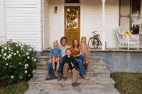 a family poses on the porch of an old farmhouse during their family photo session with shelly voss