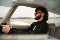 Senior portrait at a small hangar near Mobile International Airport in Mobile, Alabama — sitting
in the cockpit holding the yoke, wearing aviators.