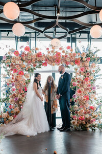 Bride and groom smile at eachother while their officiant speaks