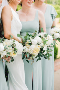 bridemaids standing next to bride holding white flowers in soft green dresses